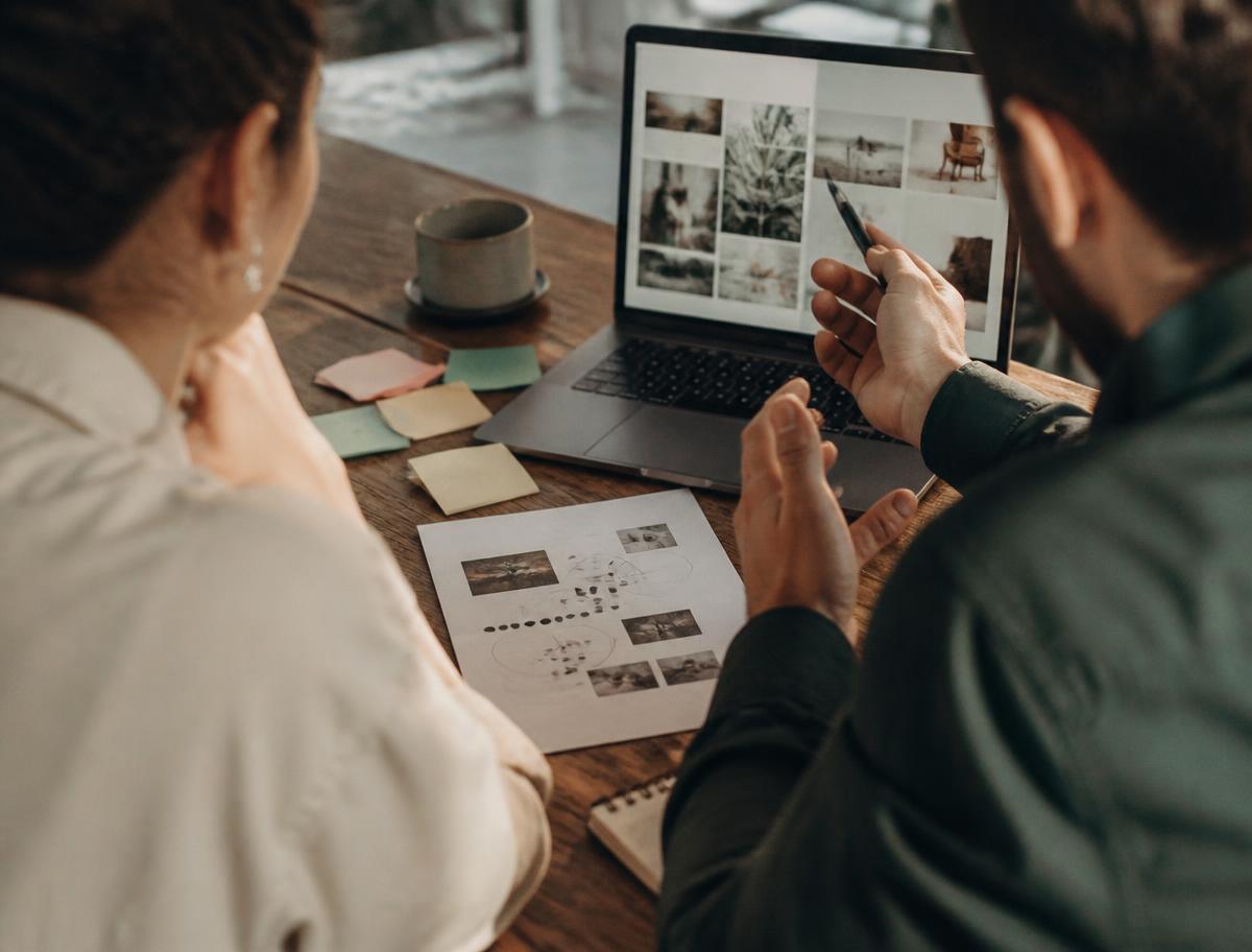 Two colleagues at a wooden table working through a printed worksheet beside an open laptop